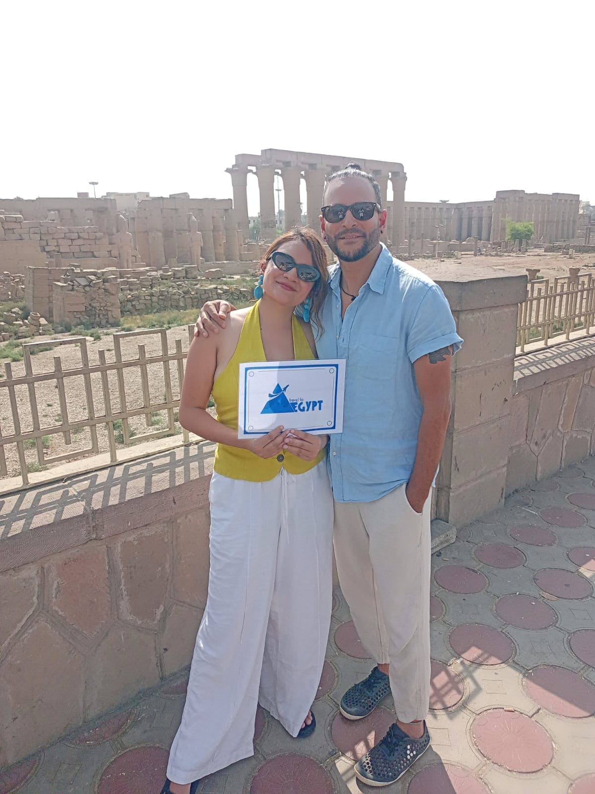 Couple holding the Travel To Egypt sign with the colonnade of Luxor Temple behind them