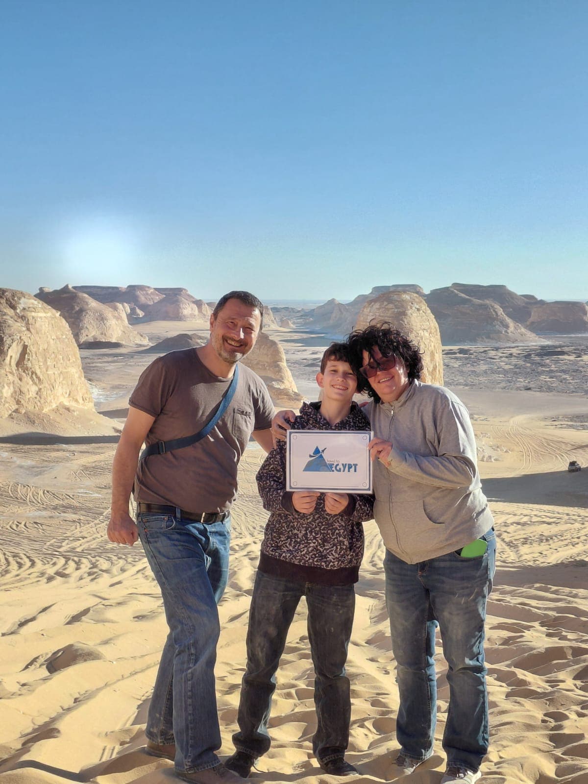 Family holding the Travel To Egypt sign among the chalk rock formations of the White Desert